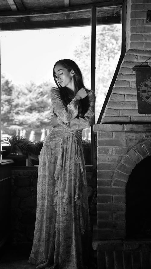 A woman in a long dress leaning against a brick wall