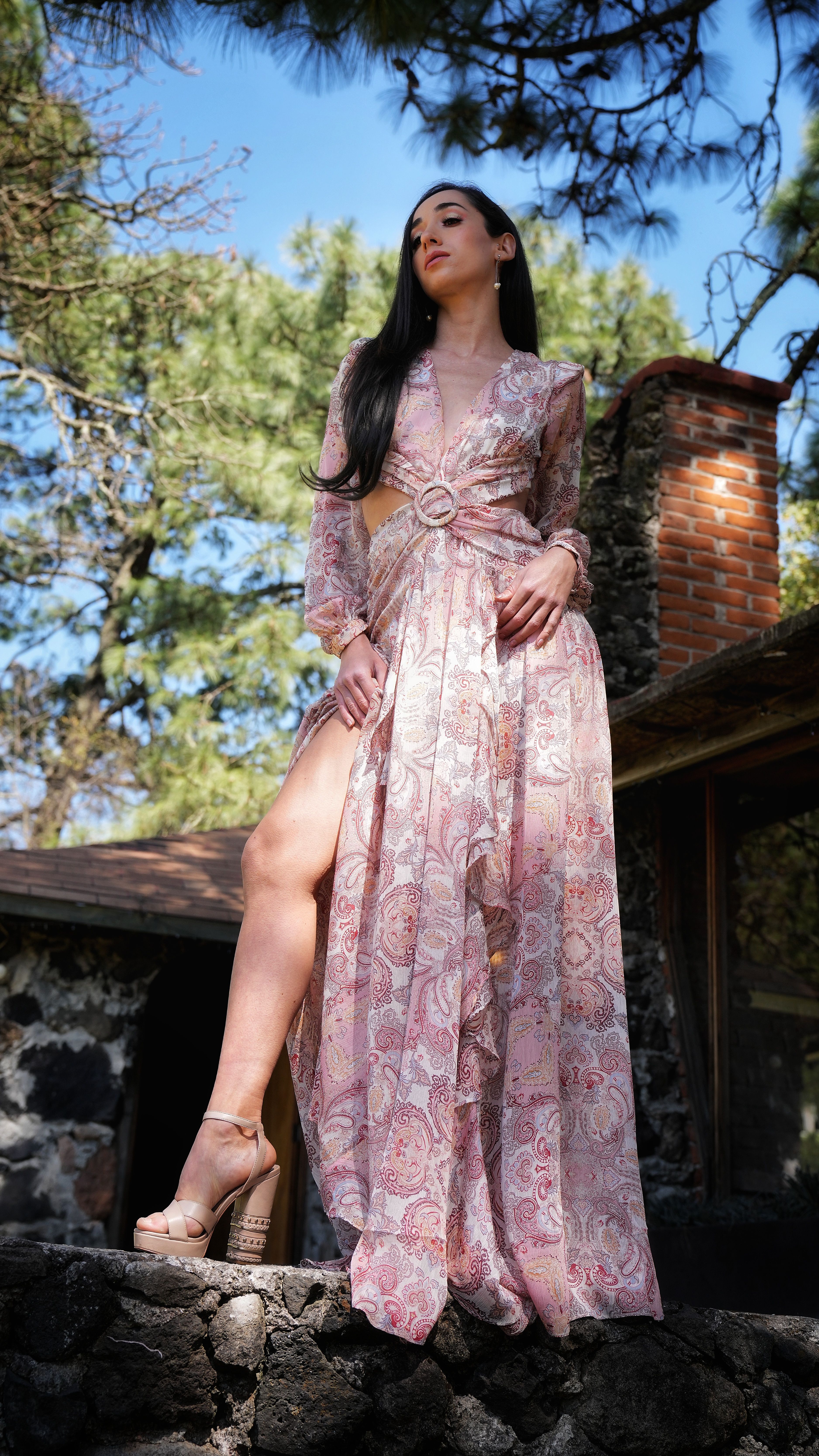 A woman in a pink dress elegantly posing outdoors in a forest setting in Mexico.