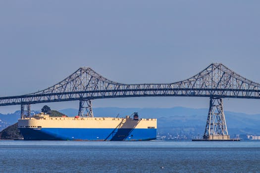 A large cargo ship sails under a steel bridge on a clear day.