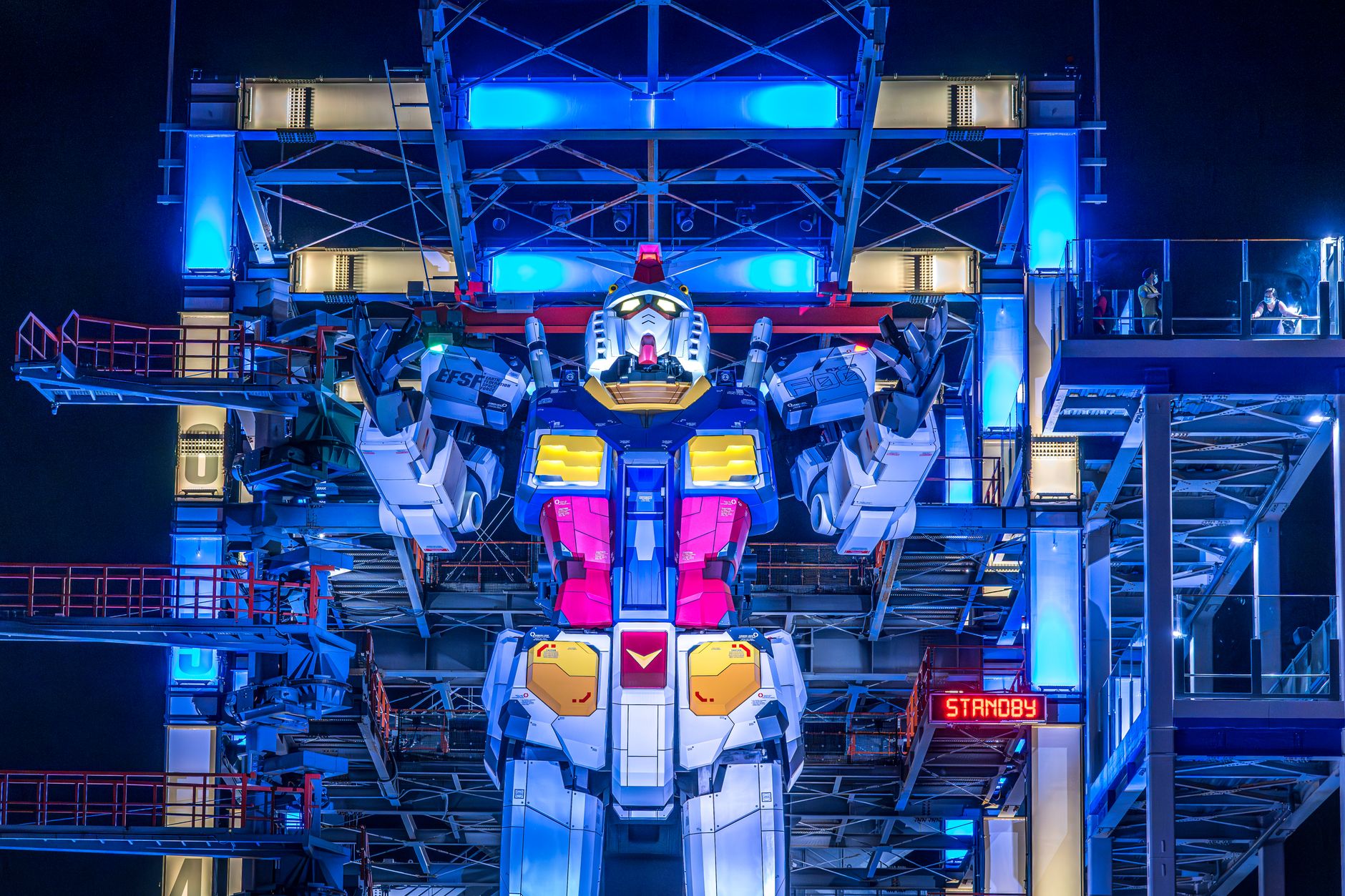 Illuminated Gundam robot at Yokohama's Gundam Factory lit up at night. Vibrant colors and futuristic design.