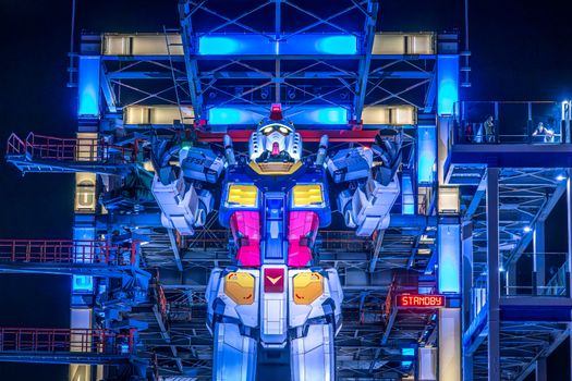 Illuminated Gundam robot at Yokohama's Gundam Factory lit up at night. Vibrant colors and futuristic design.