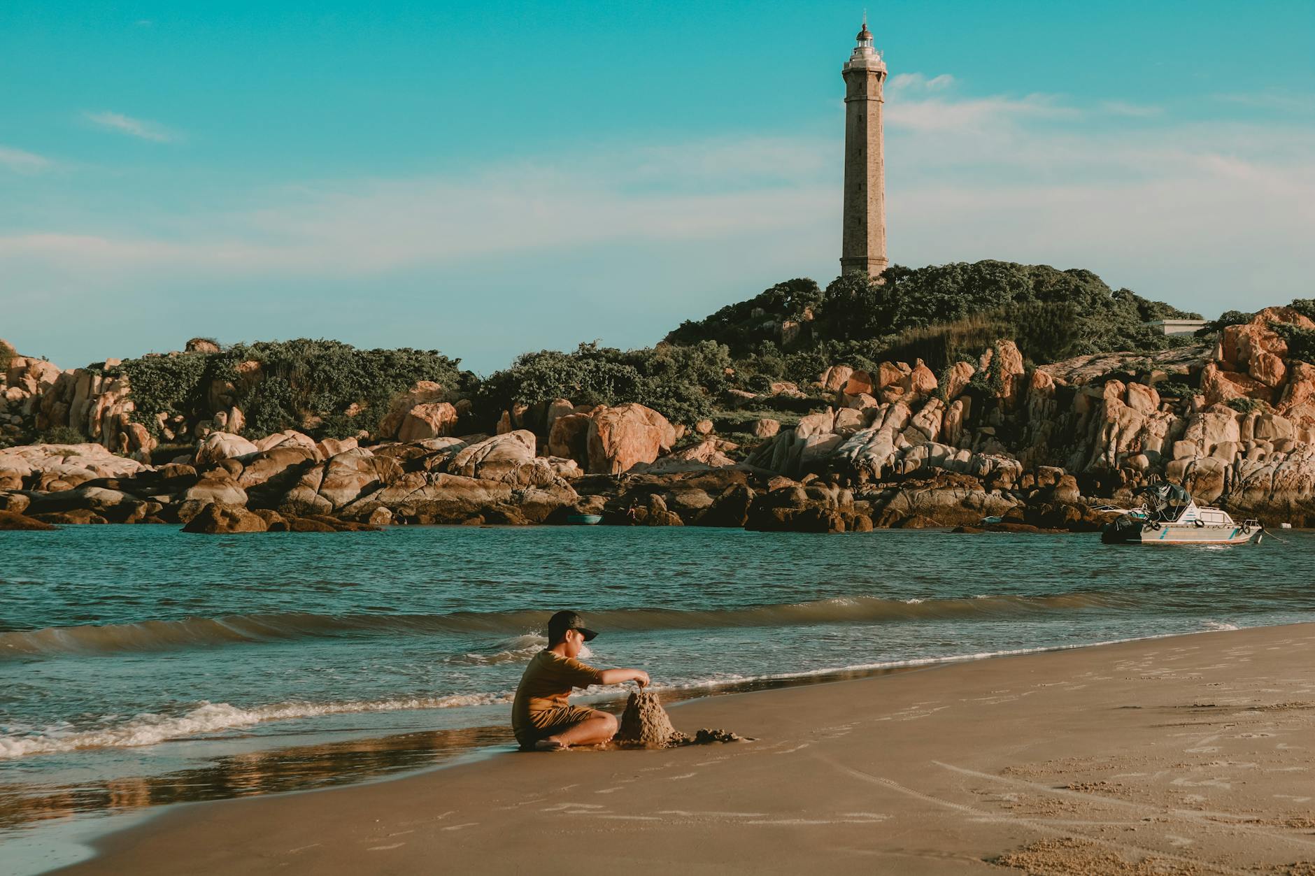 A child building sandcastles on Ke Ga Cape beach with a lighthouse in the background, Phan Thiết, Vietnam.