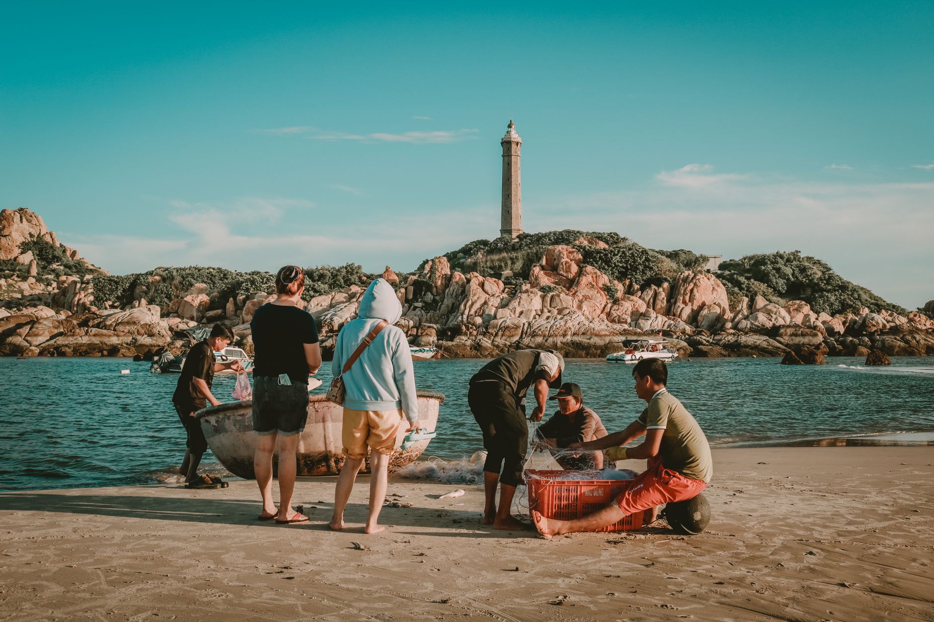 Fishermen collecting nets on a sandy beach in Phan Thiết, Vietnam, under a clear sky.