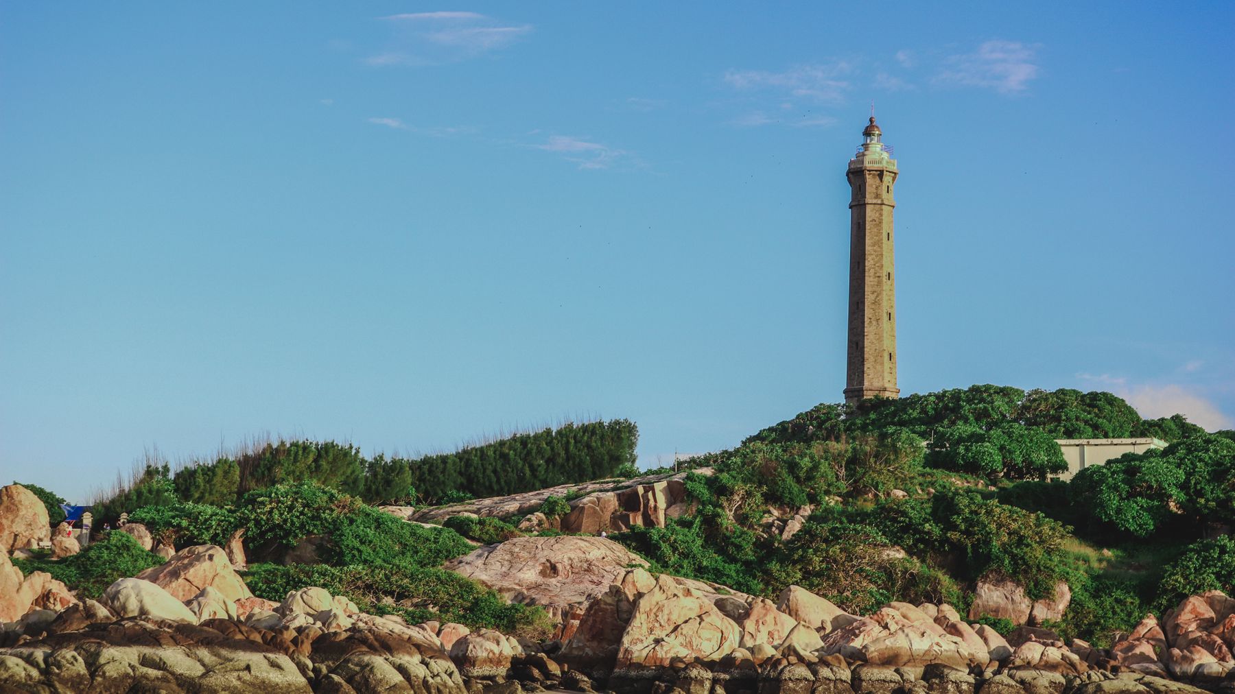 Scenic view of Ke Ga Lighthouse surrounded by lush greenery and rocky coastline in Phan Thiet, Vietnam.
