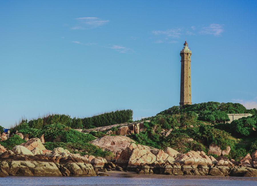 Scenic view of Ke Ga Lighthouse surrounded by lush greenery and rocky coastline in Phan Thiet, Vietnam.