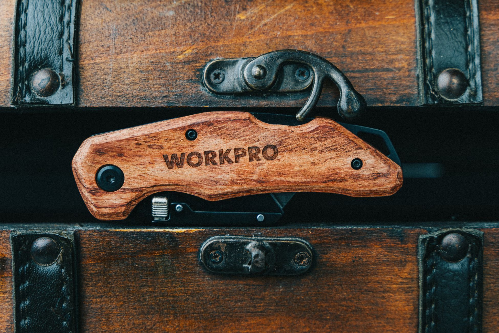 Close-up of a wooden multi-tool knife set against an antique chest, showcasing craftsmanship.