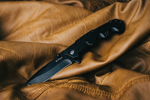 A sleek black folding knife on a textured brown leather surface, showcasing its design.