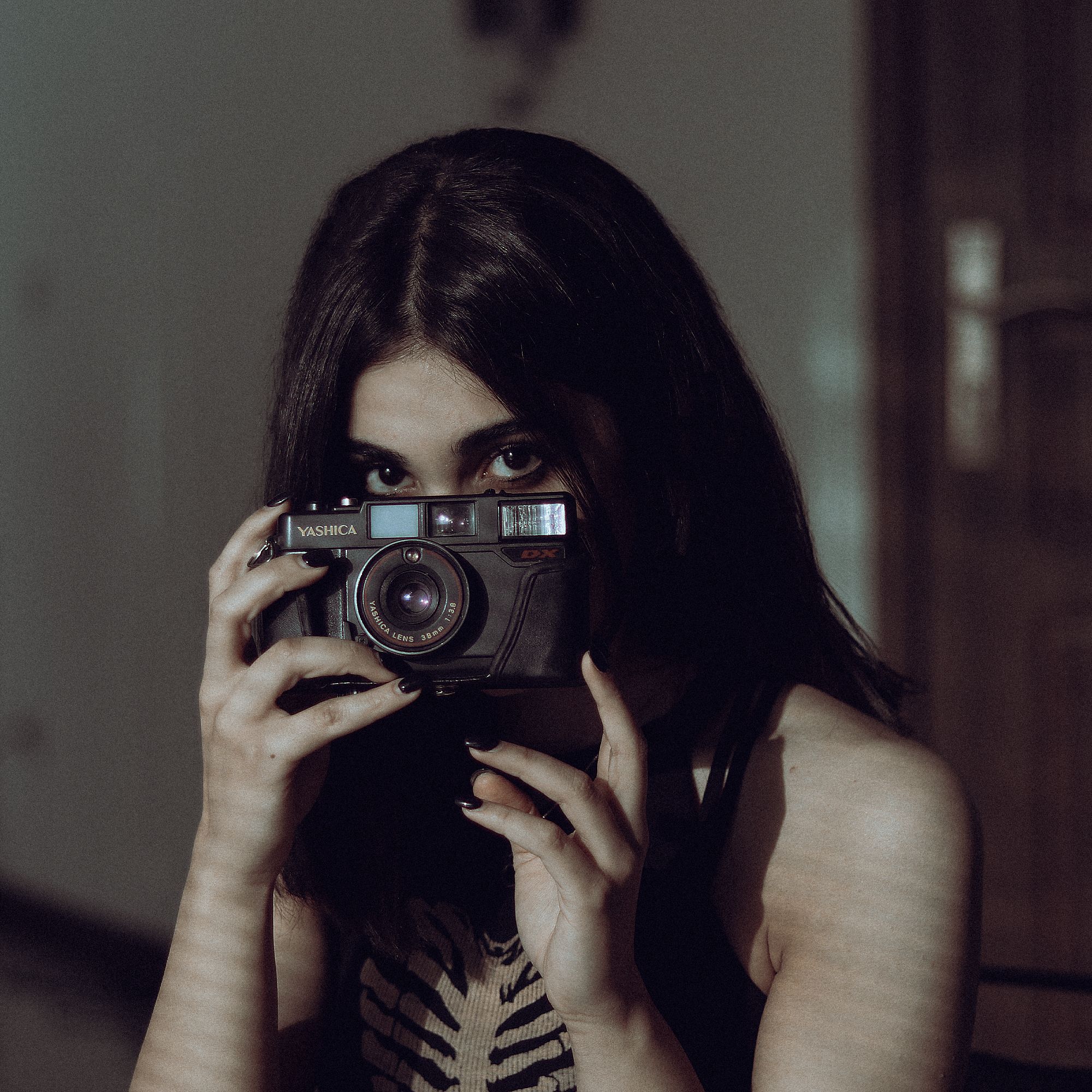 A young woman holding a vintage film camera, capturing creativity with a mysterious and artistic gaze.