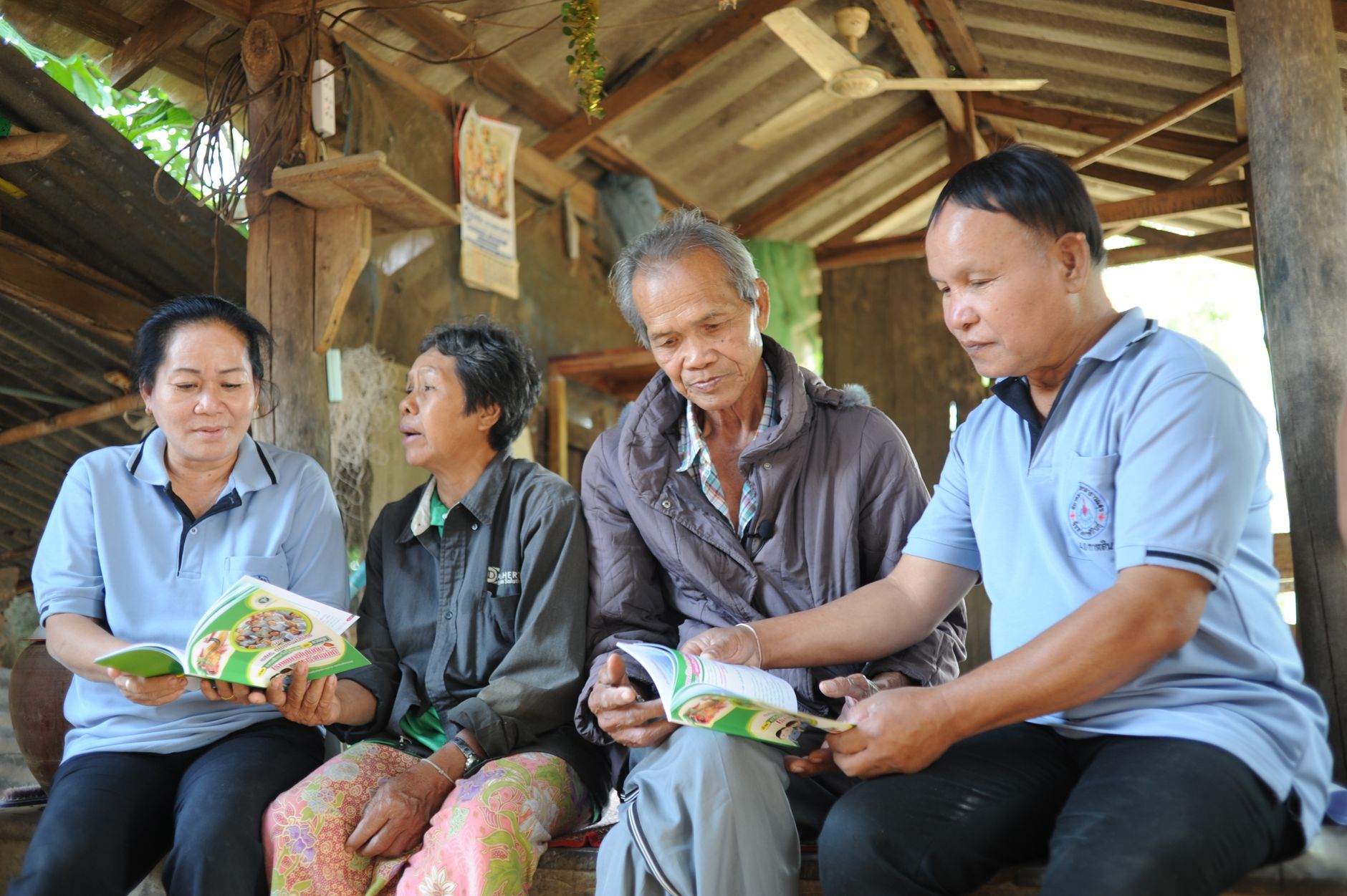 A group of senior adults reading booklets together in a rustic wooden outdoor setting.
