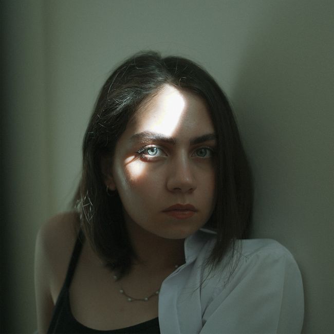 Portrait of a woman with short black hair in dramatic lighting creating shadows.