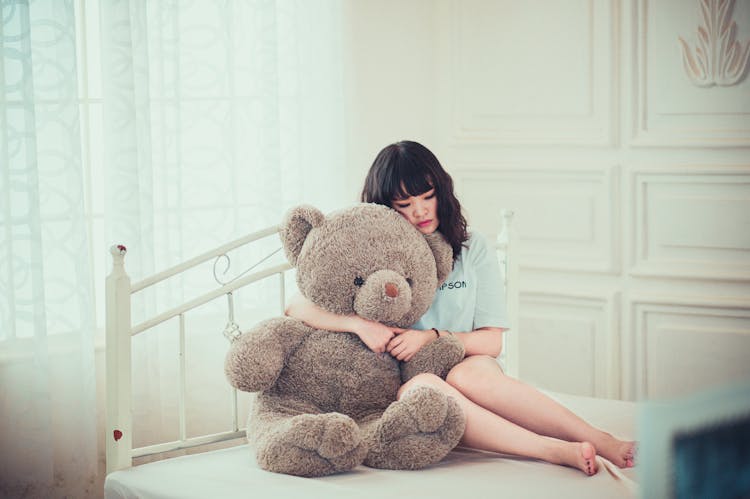 Woman Hugging Gray Bear Plush Toy On White Mattress