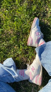 Close-up of fashionable New Balance sneakers and jeans in a sunny park setting.