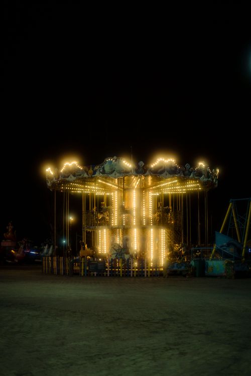 Free A glowing carousel illuminates the night at an amusement park, creating a magical atmosphere. Stock Photo