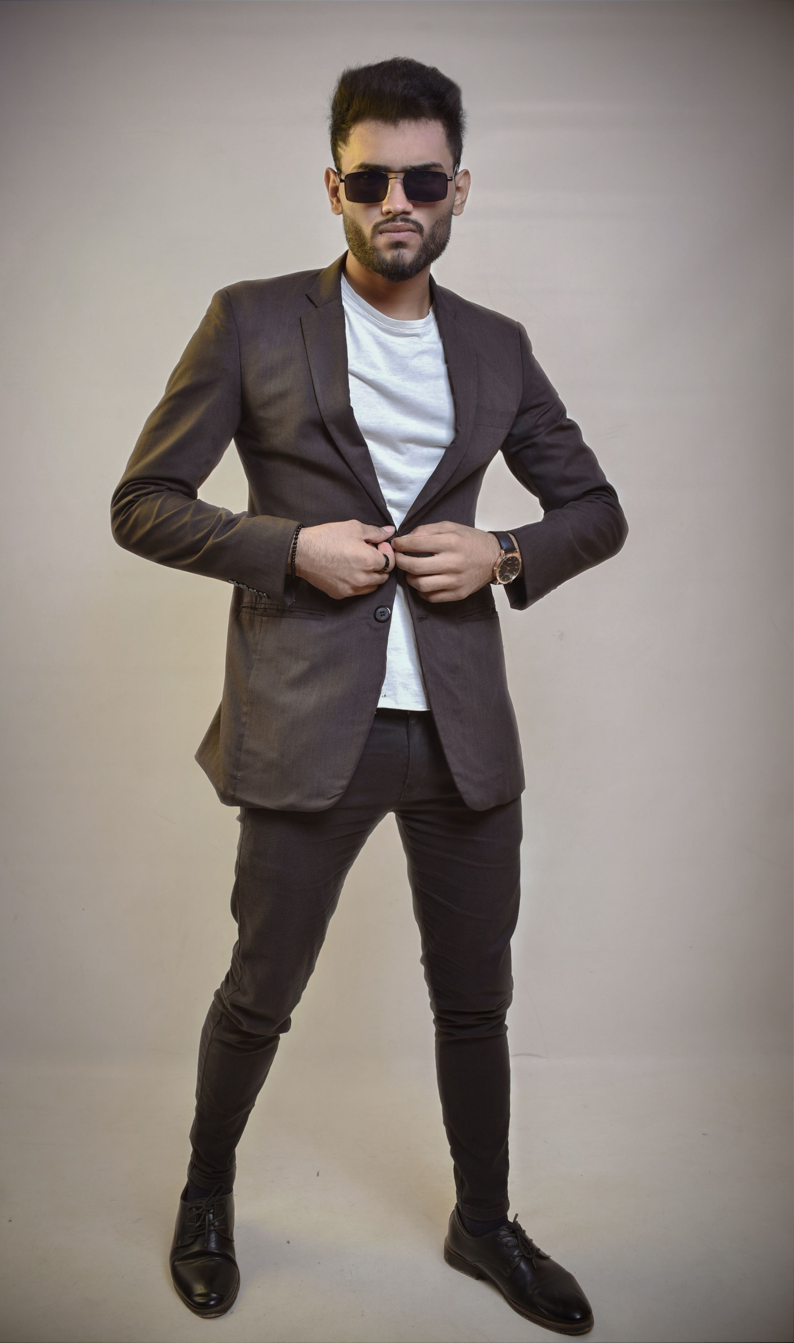 Fashion-forward man in a blazer and sunglasses strikes a confident pose. Studio shot.