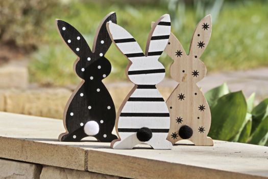 Three wooden rabbit figurines with unique patterns sit on a stone ledge outdoors, perfect for Easter decor.