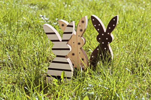 Three wooden bunny decorations on green grass, perfect for Easter themes.