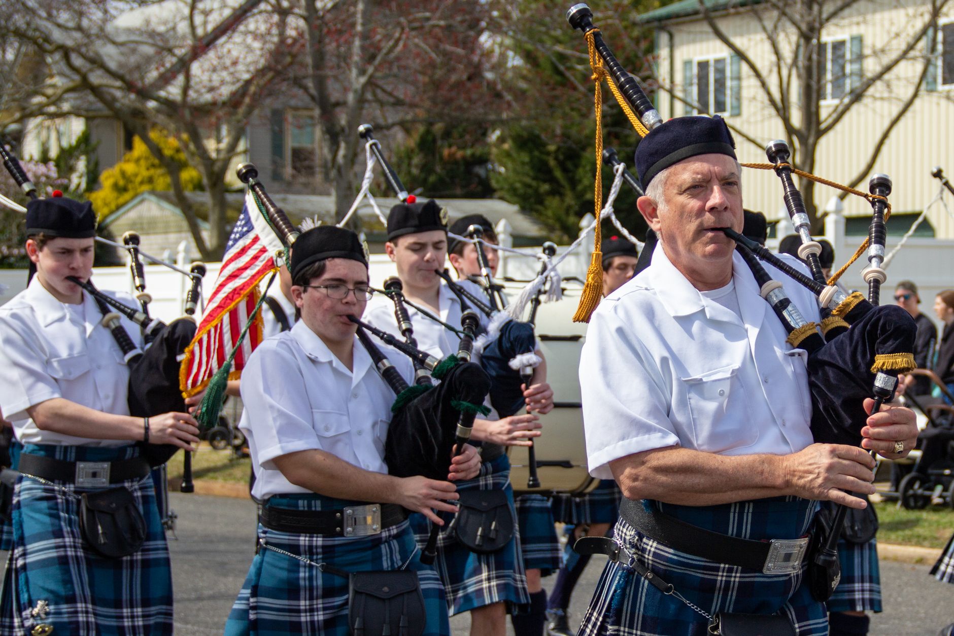 A group of bagpipers in kilts perform in a vibrant street parade.
