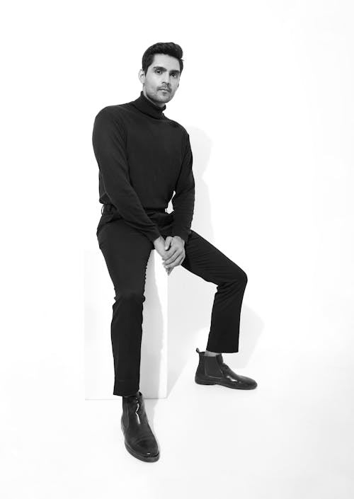 A man in black turtleneck and black pants sitting on a white block