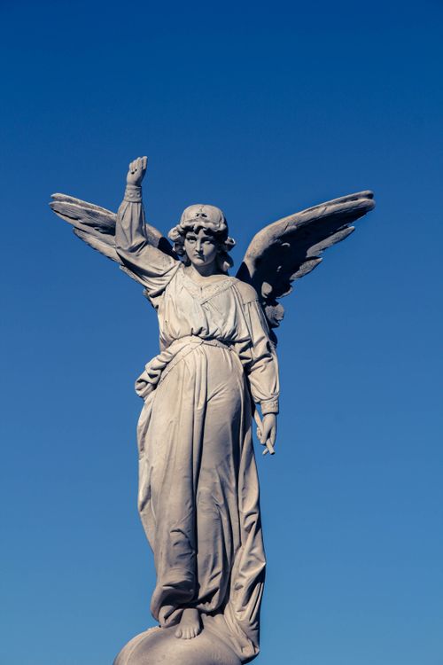 Free Elevated view of an angel statue with wings spread, set against a vibrant blue sky. Stock Photo