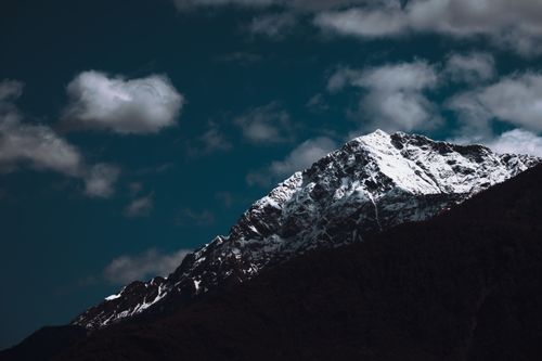 Free Stunning view of a snow-capped mountain peak with dramatic clouds in a clear blue sky. Stock Photo