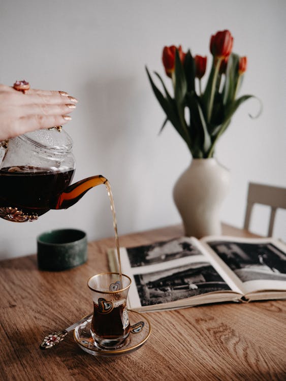 Woman Pouring Tea from a Glass Pot into a Glass