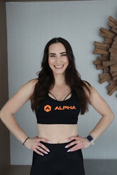 Smiling woman in fitness attire poses confidently with a smartwatch on a neutral background.