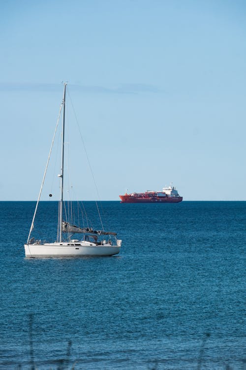 A sailboat in the ocean with a large ship in the background