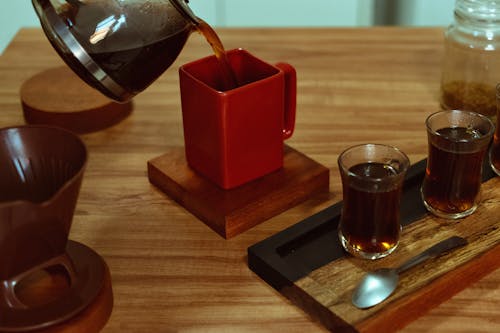 A coffee pot is being poured into cups on a wooden tray