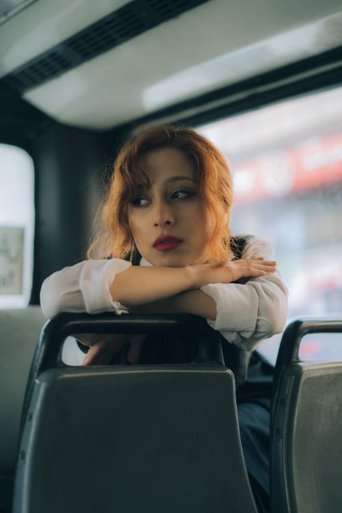 Free Portrait of a woman with red hair leaning on bus seats in Tehran, showcasing modern urban life. Stock Photo