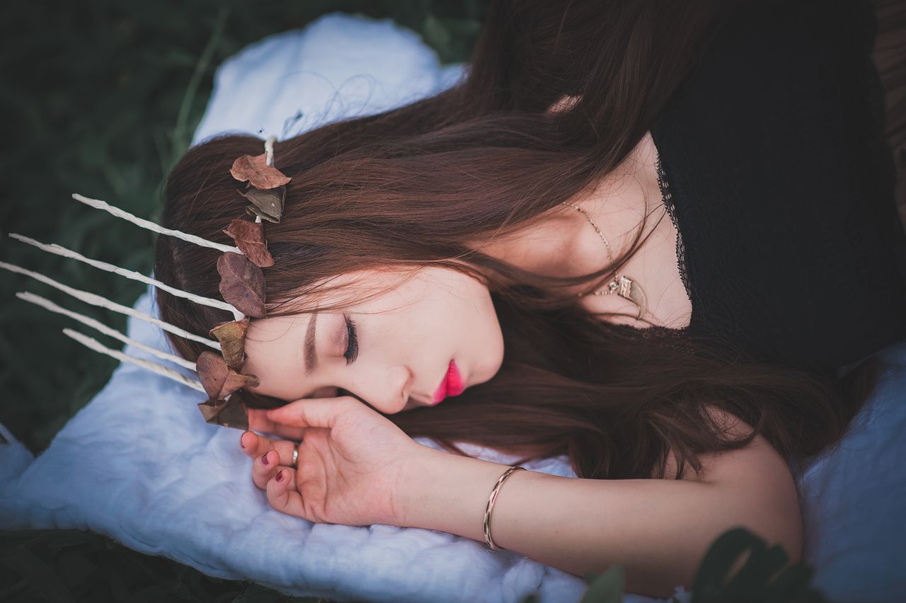 a serene woman with a leaf crown lies asleep on a soft blanket outdoor