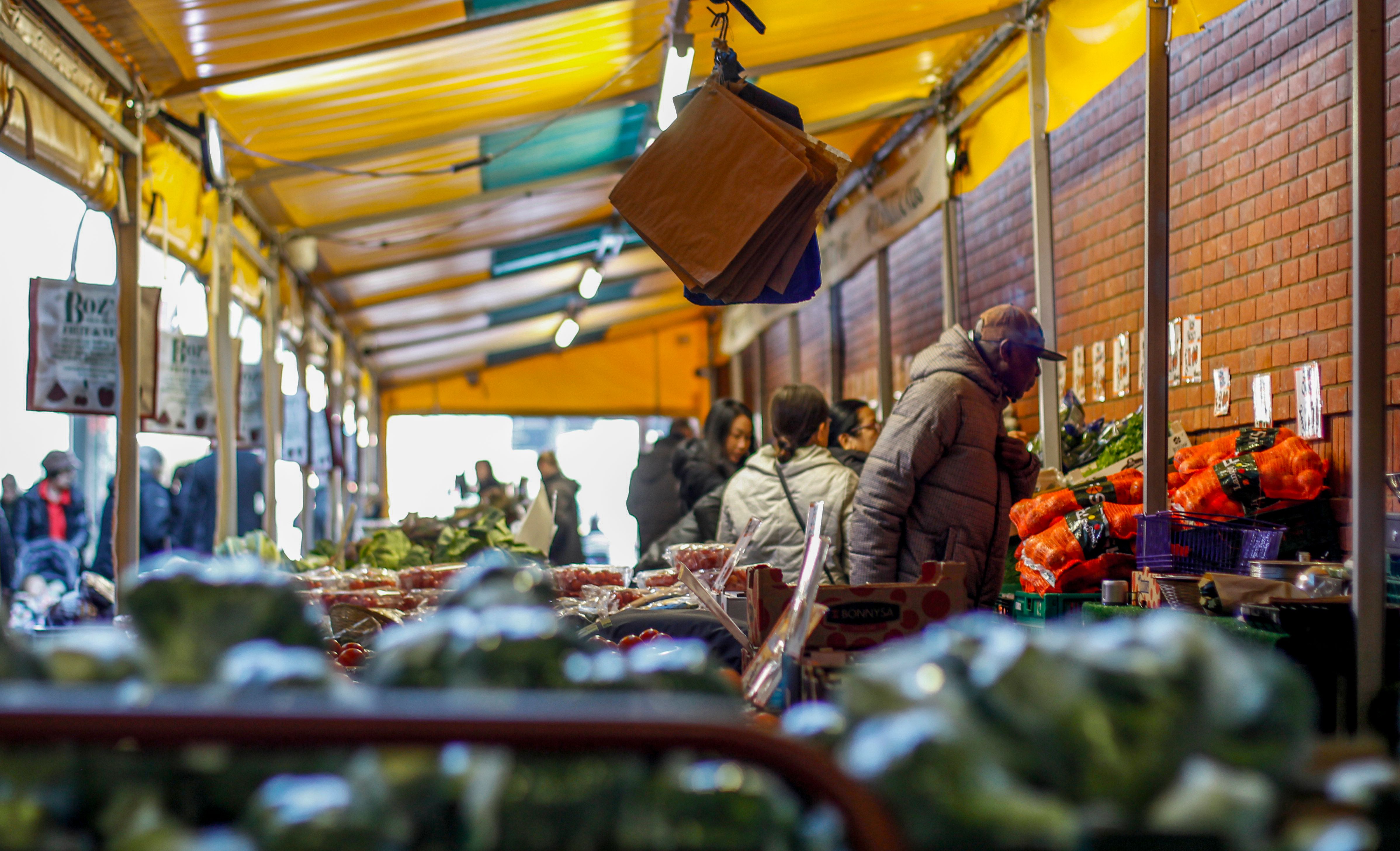 A vibrant marketplace filled with people shopping for fresh vegetables under a colorful canopy.
