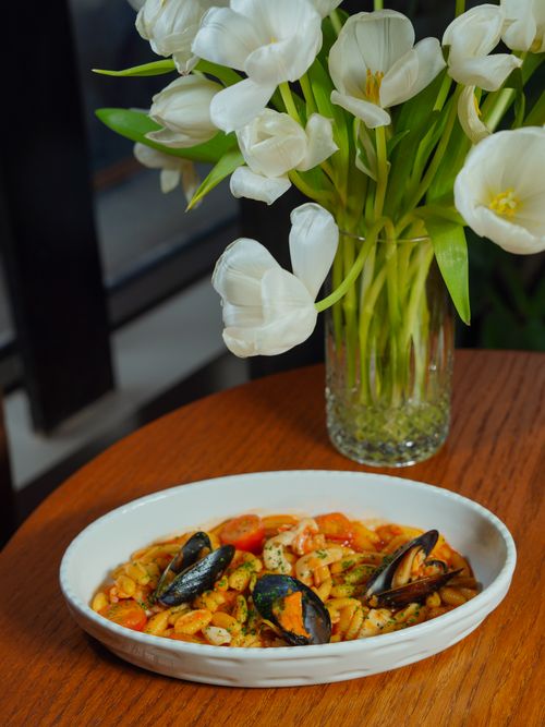 Free Delicious seafood pasta dish beside a vase of fresh white tulips on a wooden table. Stock Photo