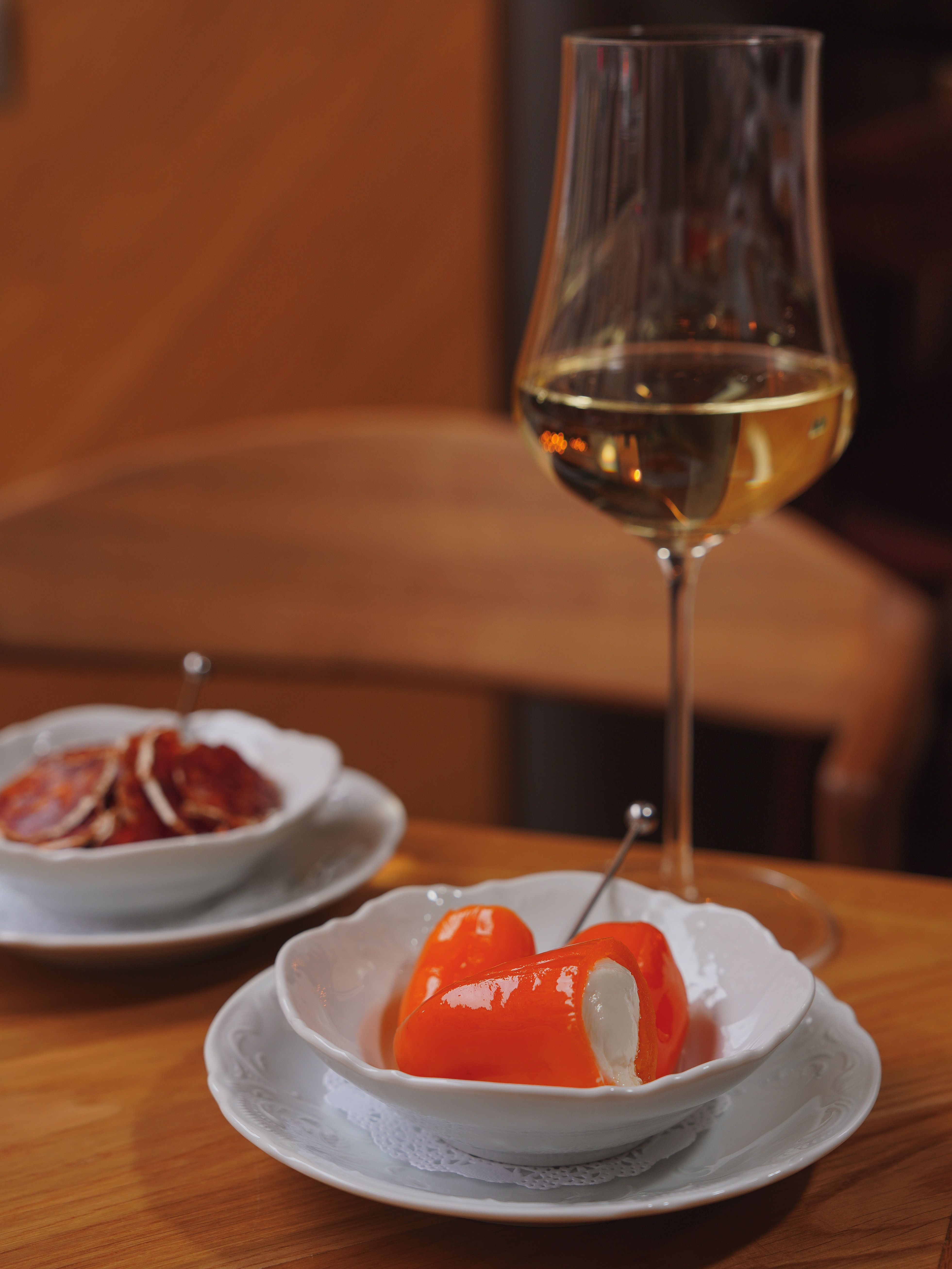 A glass of white wine paired with piquillo peppers and sliced meat, perfect for gourmet dining.