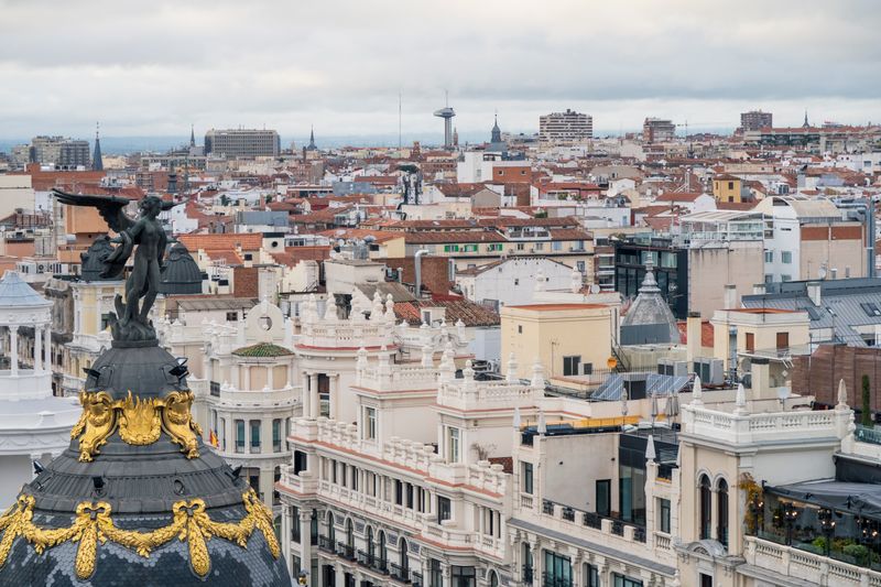 Rooftops along Gran Vía in Madrid with the domed Metropolis Building and a pale sky.