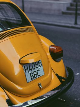 Rear view of a yellow vintage car parked on a city street, showcasing its classic design.