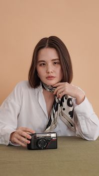 Woman in white blouse posing with vintage camera, wearing polka dot scarf.