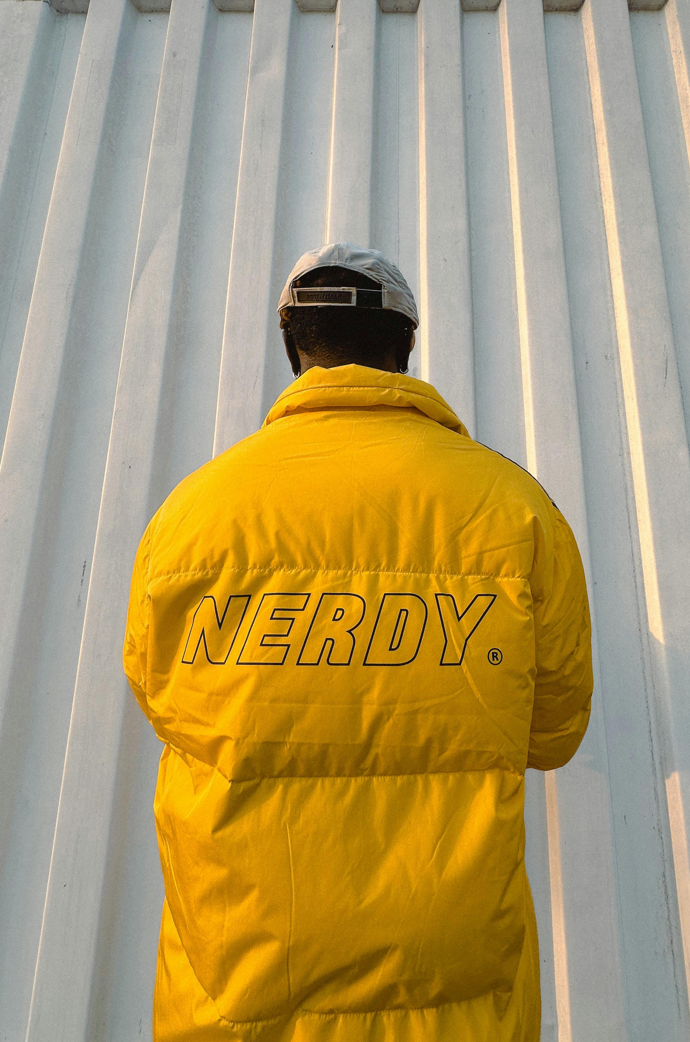 Back view of a man in a yellow 'NERDY' jacket, showcasing street fashion.