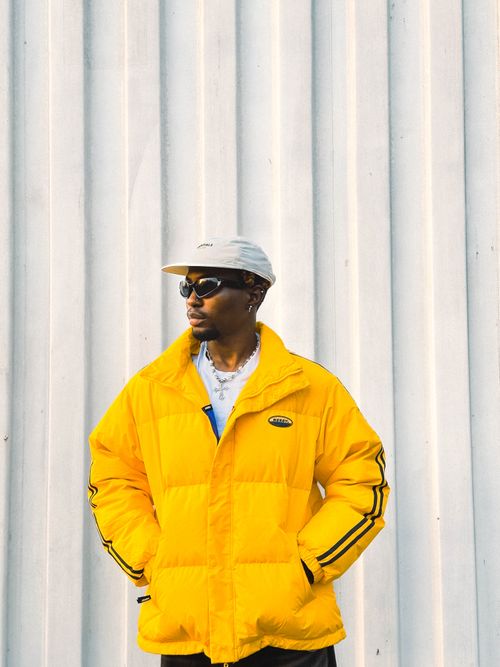 Free Fashionable young man in a yellow jacket with sunglasses standing against a textured wall. Stock Photo