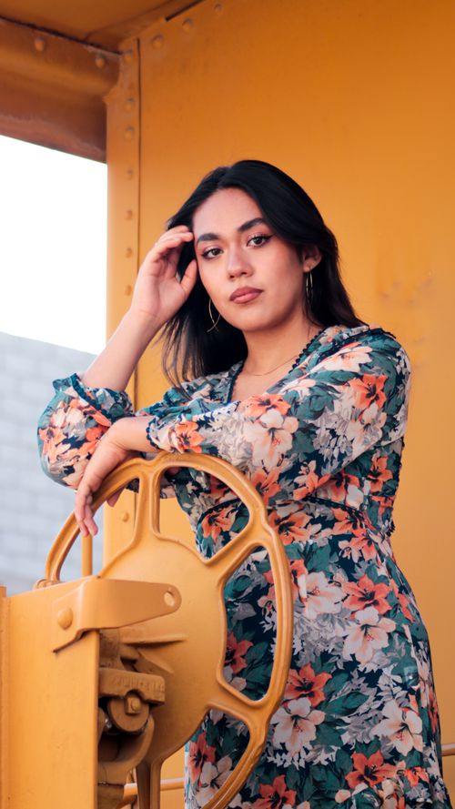 Free Portrait of a woman in a floral dress posing beside a yellow wheel in Ciudad de Apizaco, Mexico. Stock Photo