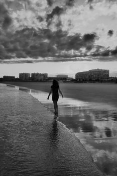 A woman walks along a lakeshore in a serene black and white scene, capturing freedom and solitude.