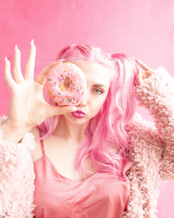 女人用粉红色的甜甜圈覆盖她的右脸