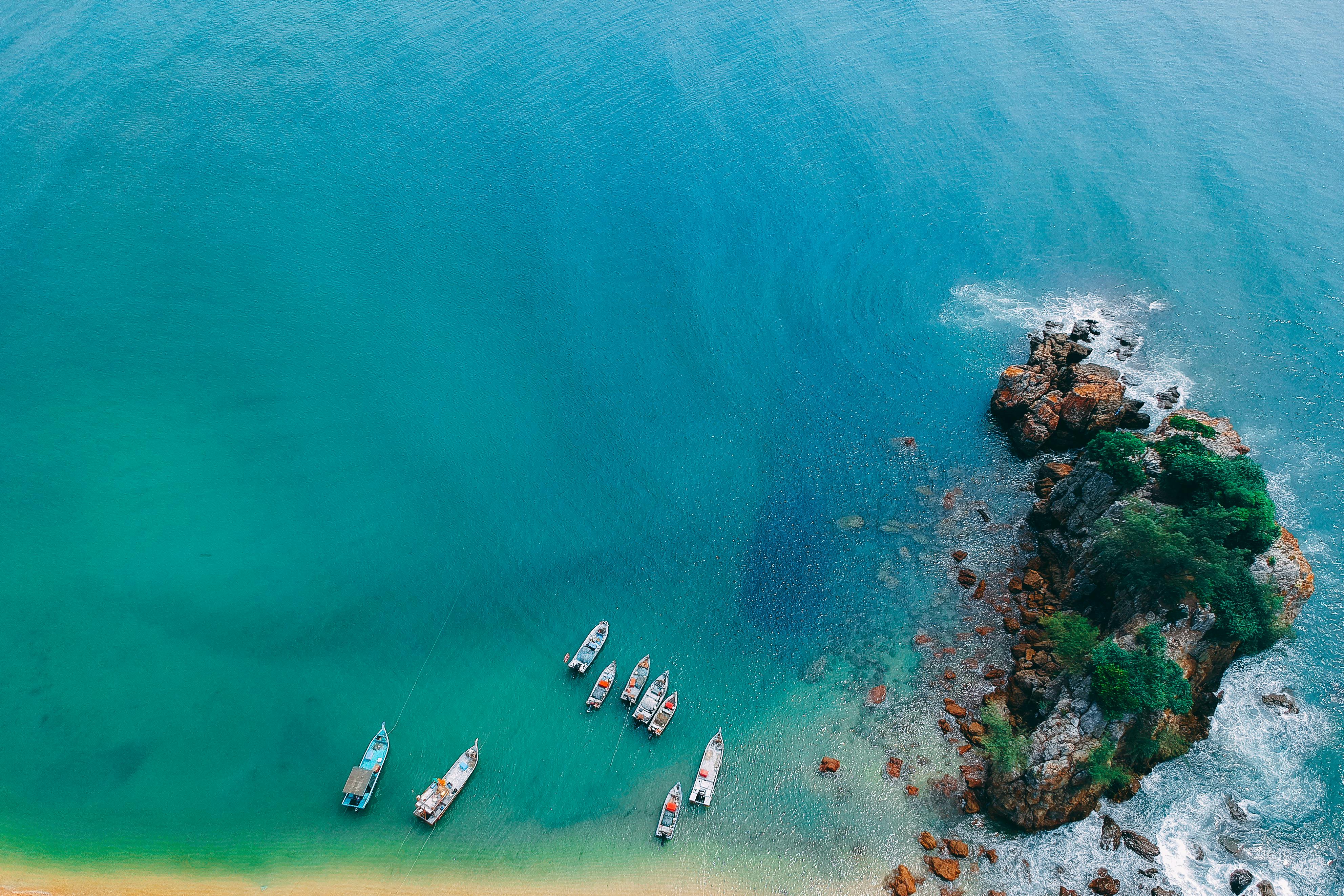 航拍镜头令人惊叹，它捕捉到了停泊在岩石热带海岸线附近、碧绿大海之畔的船只
