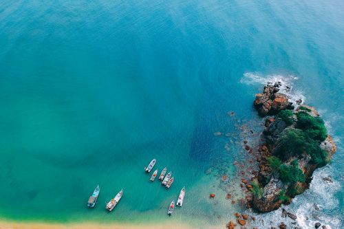 Free Stunning aerial shot of boats anchored near a rocky tropical shoreline and turquoise sea. Stock Photo