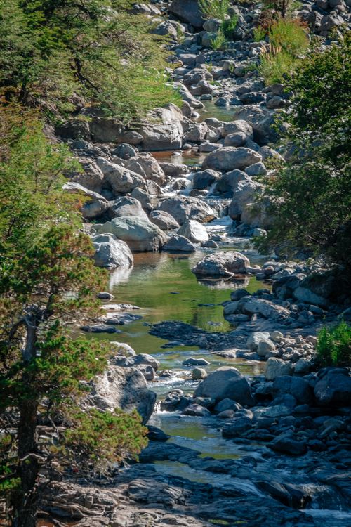 Free A tranquil river cascading over rocks in a lush mountainside, surrounded by greenery. Stock Photo