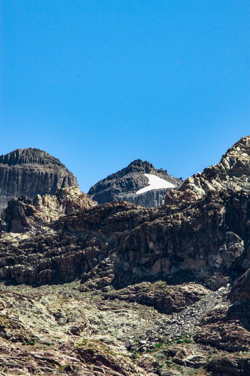 Free A breathtaking mountain landscape featuring rocky terrain and a snow-capped peak against a clear blue sky. Stock Photo