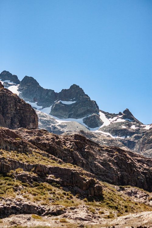 Free Rugged mountain range with snow highlights under a clear blue sky, perfect for adventure exploration. Stock Photo