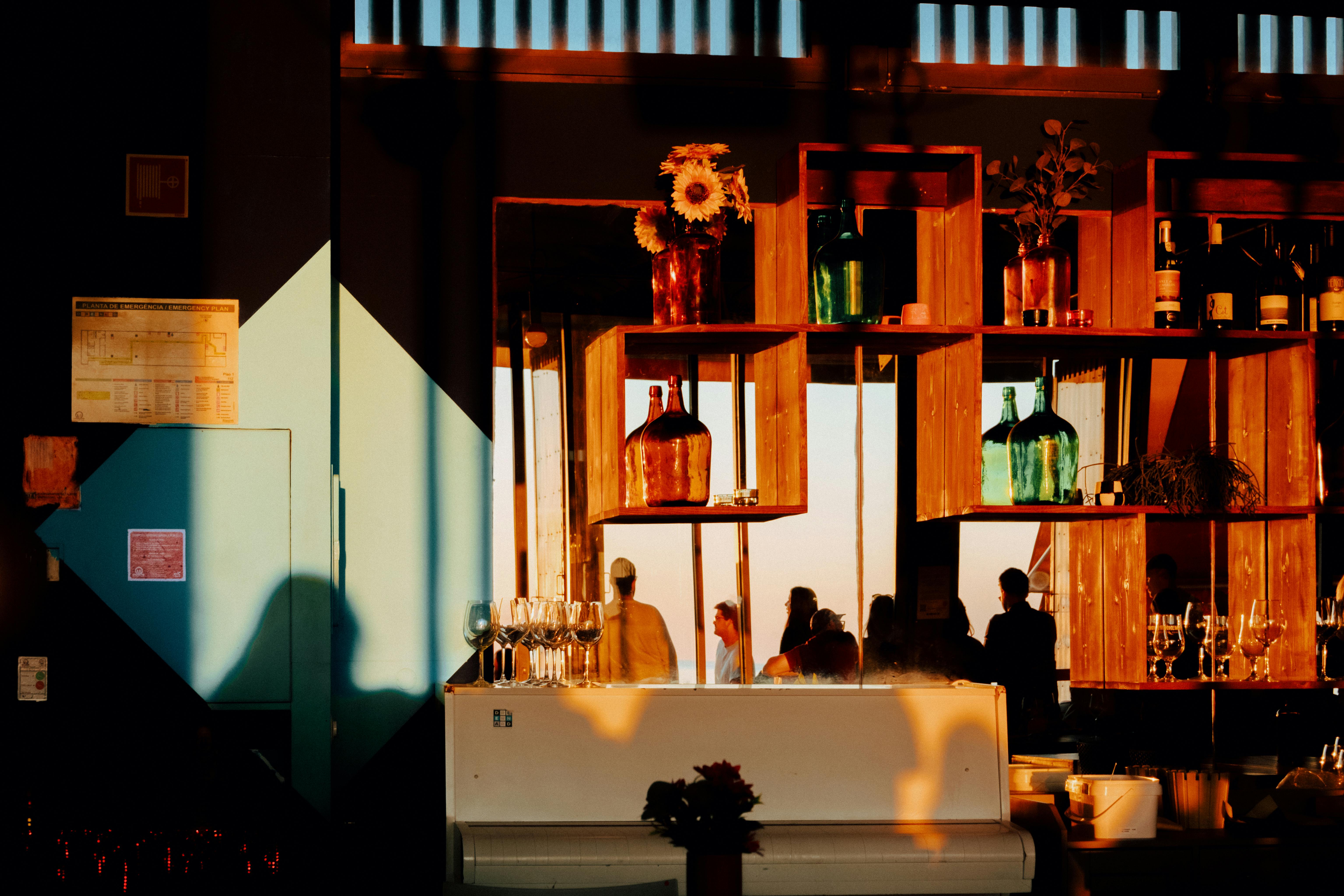Free A warm, sunlit bar in Lisboa with colorful bottles, a piano, and people silhouettes. Stock Photo