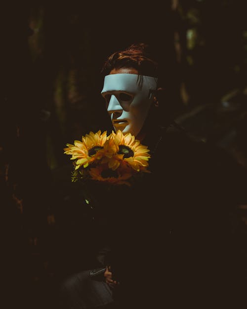 Person Wearing A Mask Holding Sunflowers