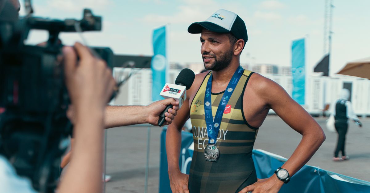 Athlete speaking at a podium with a microphone, surrounded by journalists
