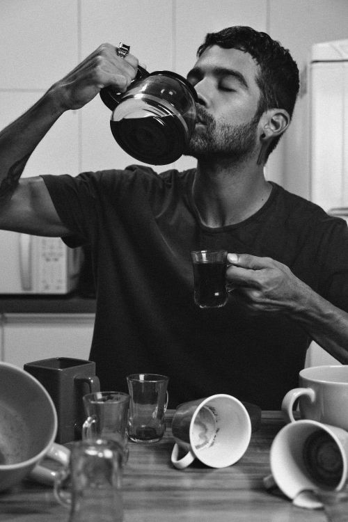 Free Black and white portrait of a man savoring coffee with an array of cups on a table, creating a vibrant yet minimalist aesthetic. Stock Photo